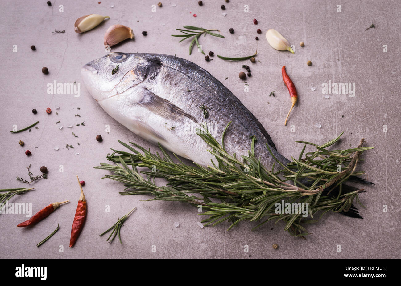 Fresh dorado fish. Dorado and cooking ingredients - rosemary, spices, garlic, thyme, herbs. Cooking concept. On light stone background. Stock Photo