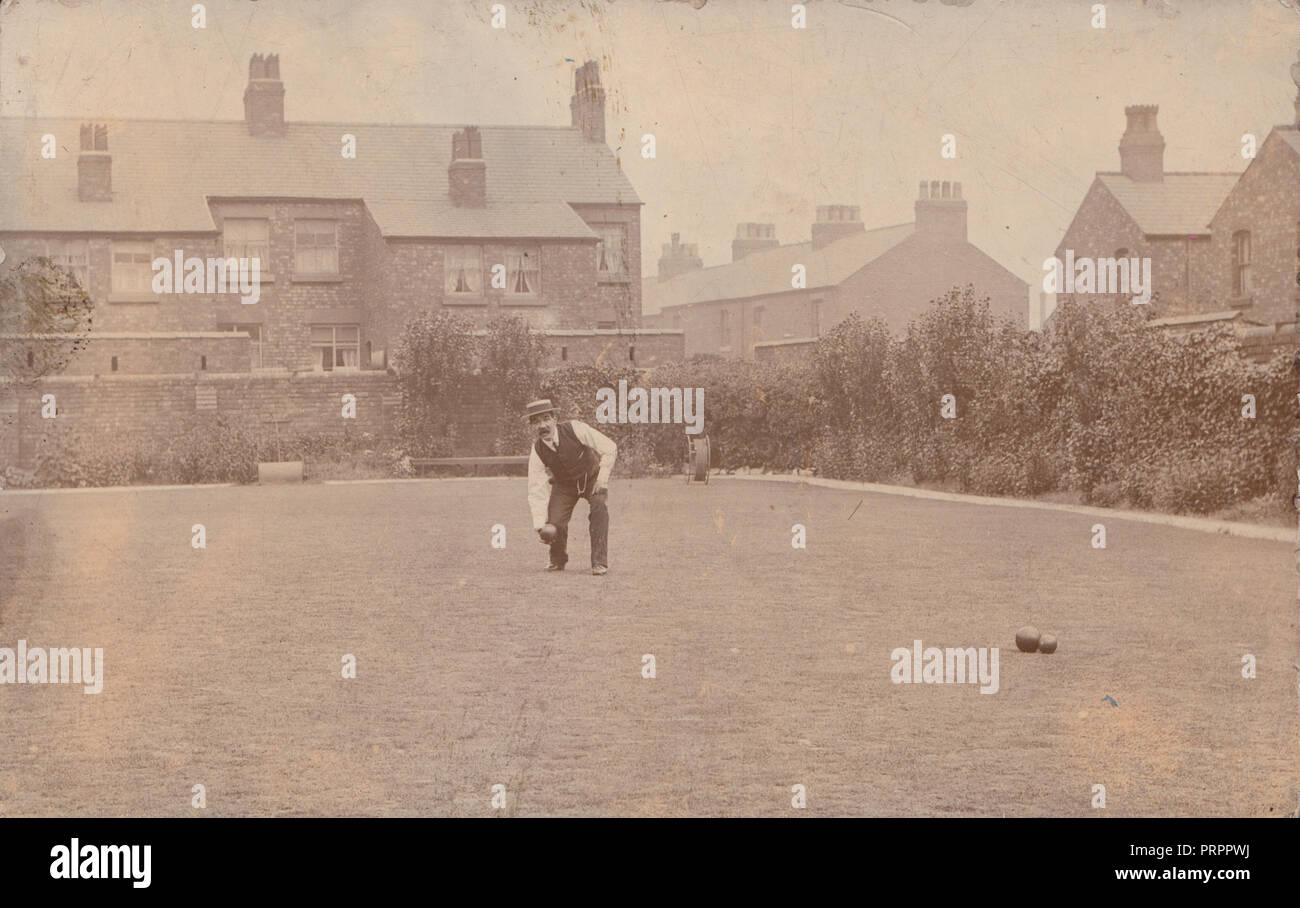 * Vintage British Photographic Postcard of a Man Playing Lawn Bowls With Terraced Housing in The Background. Stock Photo