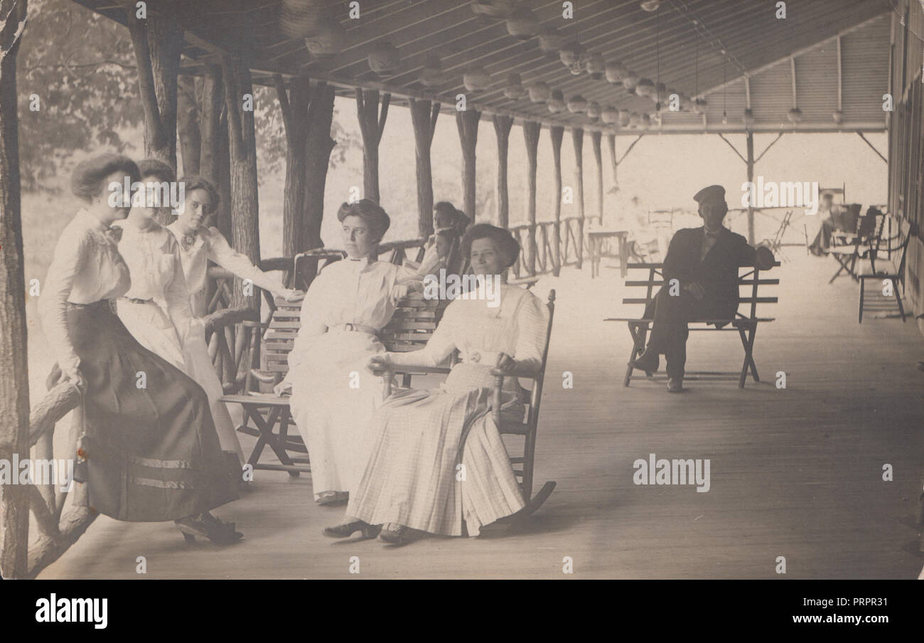 * Vintage Photograph of a Lady Sat In a Rocking Chair on a Porch In The Company of Her Female Companions or Family Stock Photo
