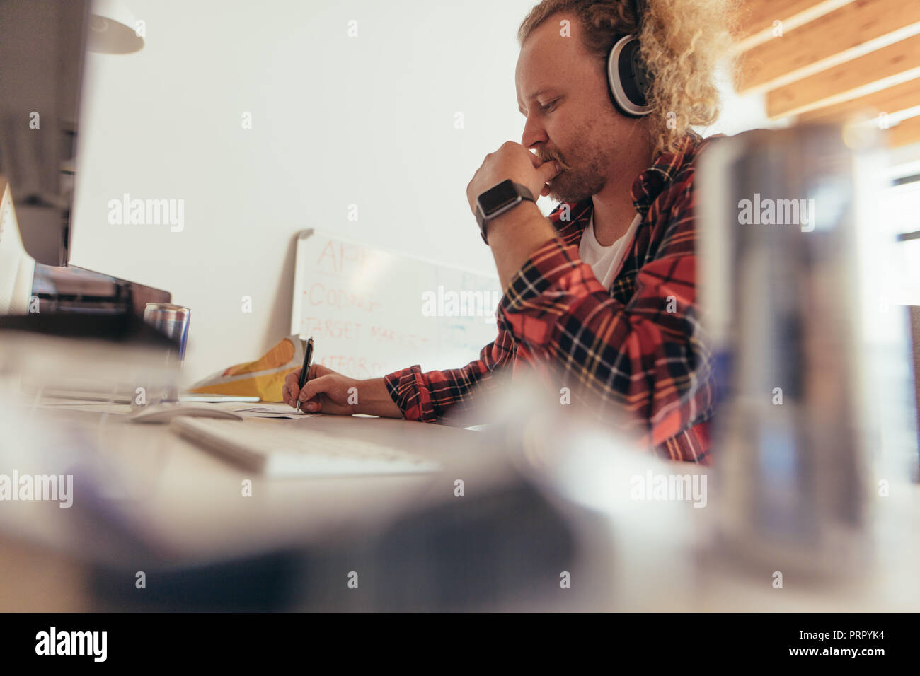 Man making some notes in copybook, sitting at small office table. Experience tech professional coding on a notepad in office. Stock Photo