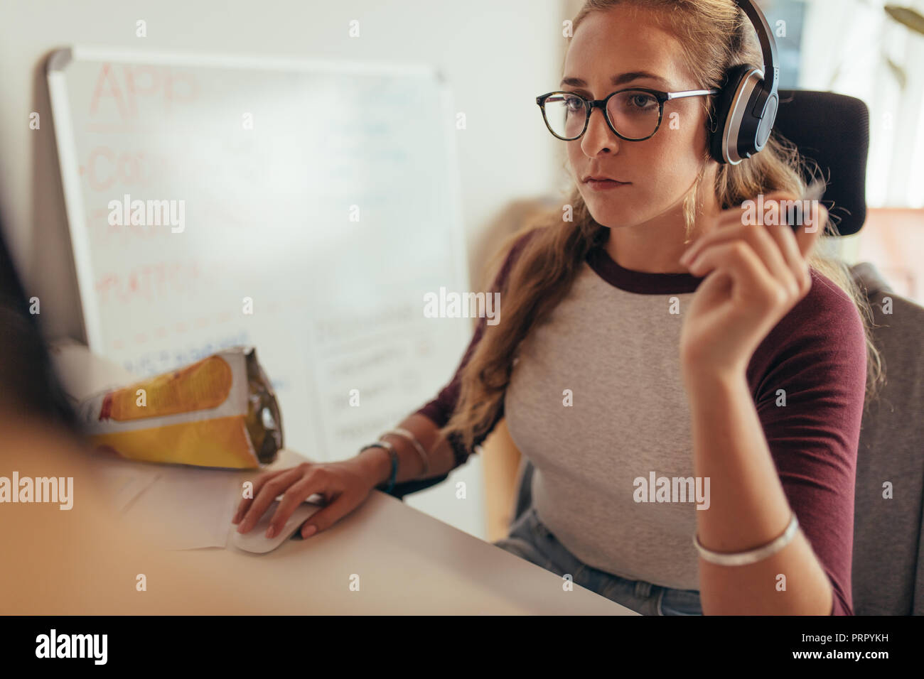 Young caucasian woman wearing headphones sitting at her desk and working on computer. Female programmer working on new software development. Stock Photo