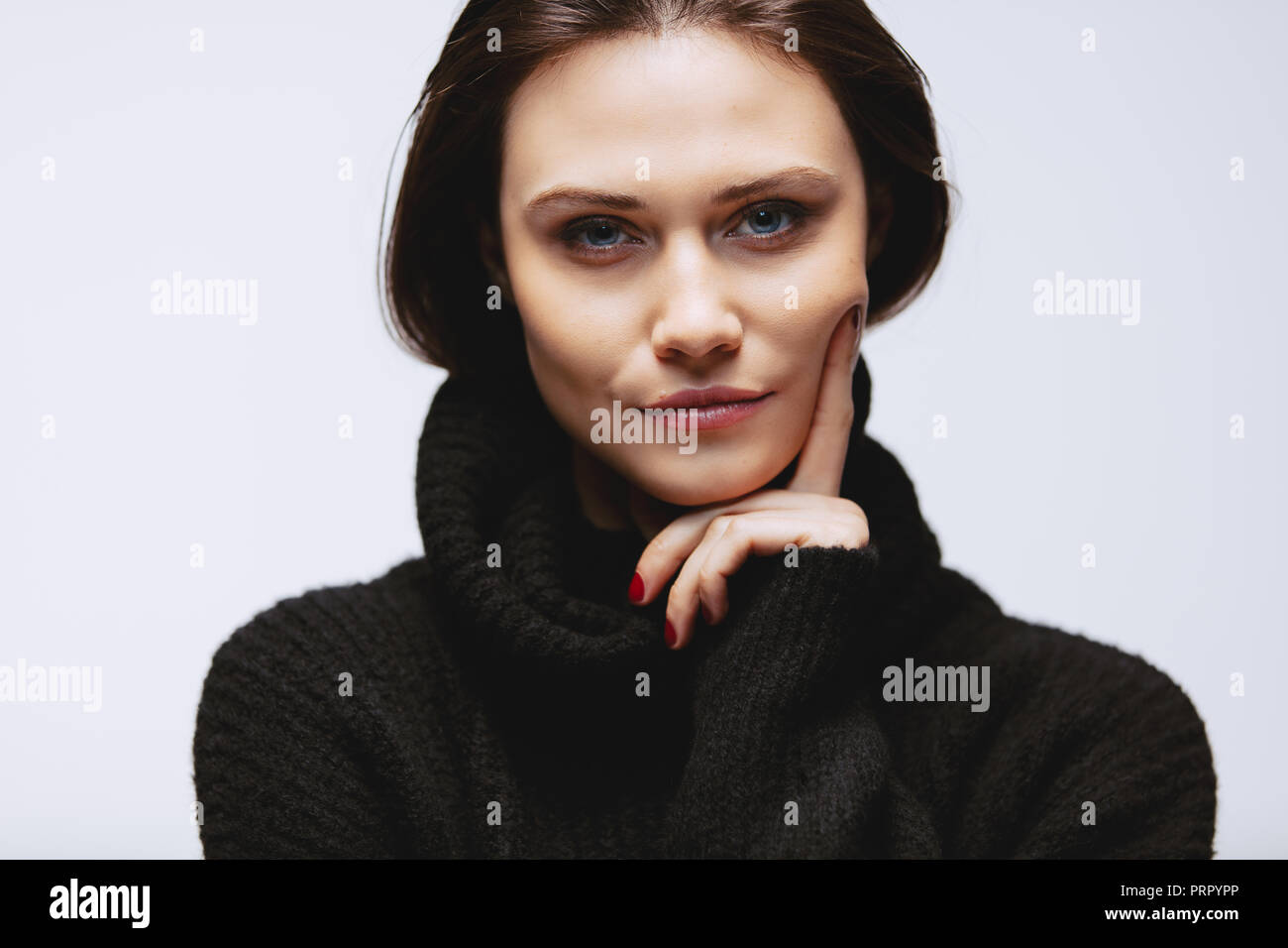 Close up portrait of beautiful woman wearing black sweater with her hand on chin. Caucasian female model staring at camera. Stock Photo