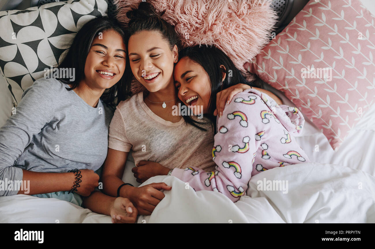 Three Girls Laughing And Having Fun While Lying On Bed Together During A Sleepover Top View Of