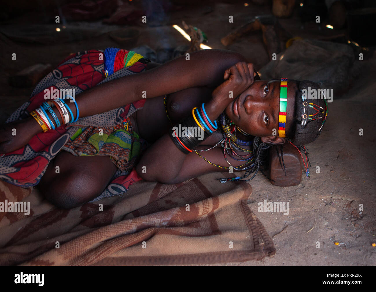 Muhacaona tribe woman resting on her wooden headrest inside her hut, Cunene Province, Oncocua, Angola Stock Photo