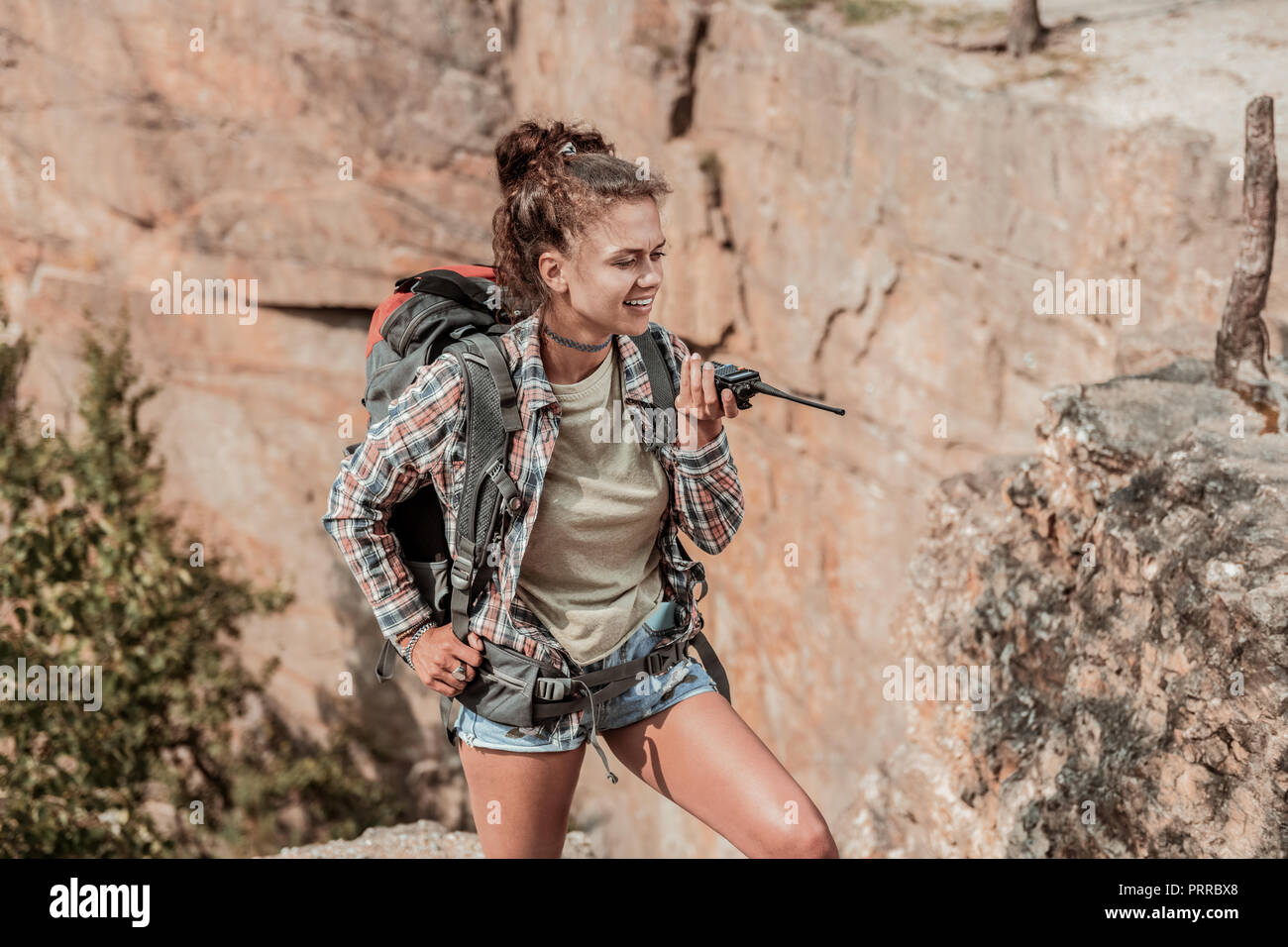 Curly beaming female hiker with big backpack contacting her company via pager Stock Photo
