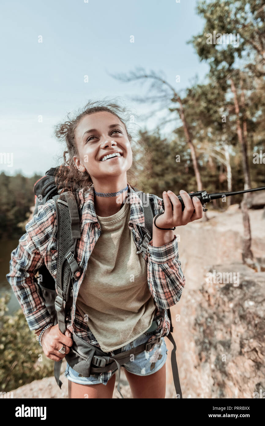 Curly beaming woman feeling happy hiking in the mountains with backpack Stock Photo