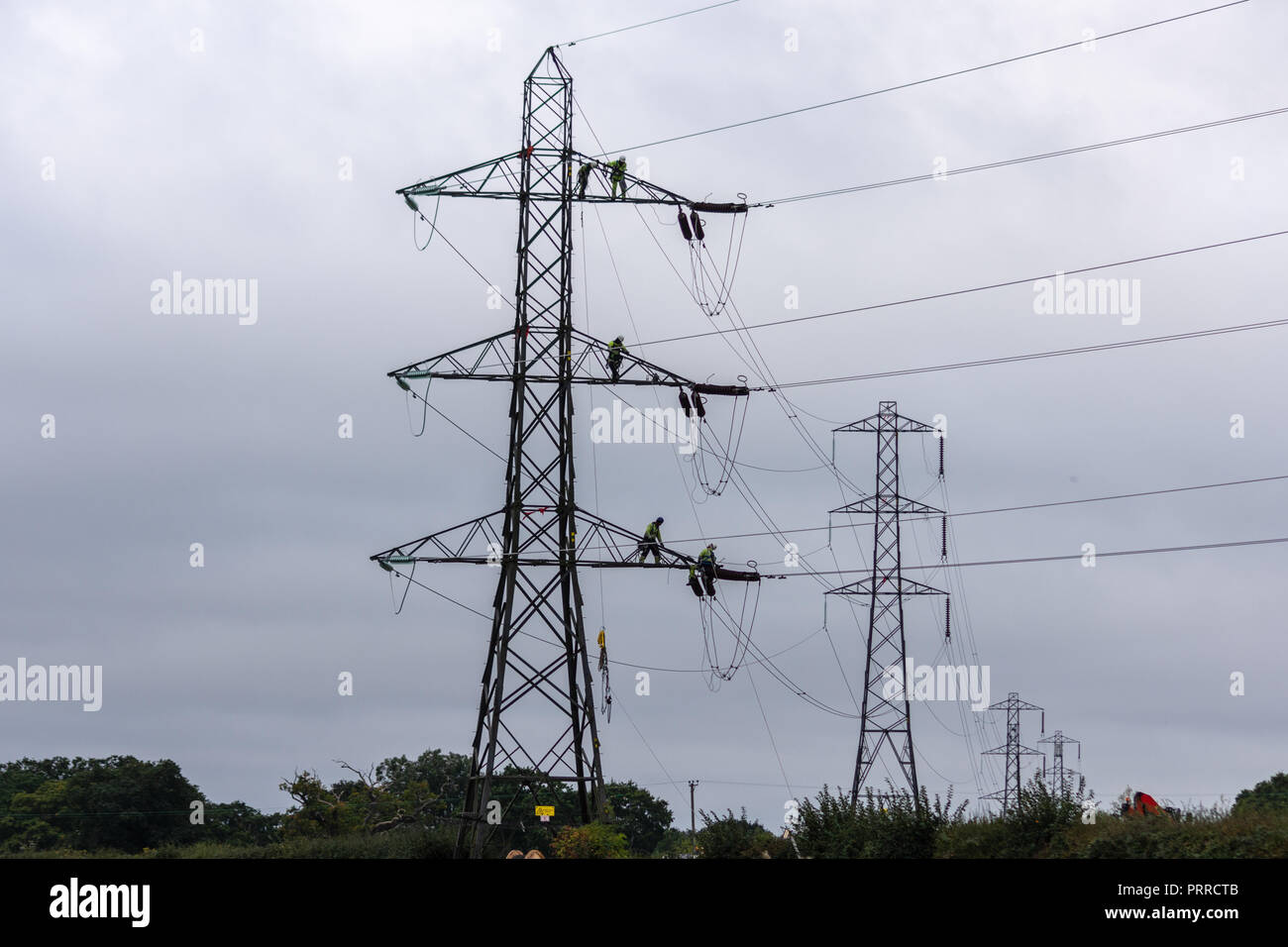Electricity workers wearing safety harnesses on an electricity pylon in the process of replacing the high voltage cables Stock Photo