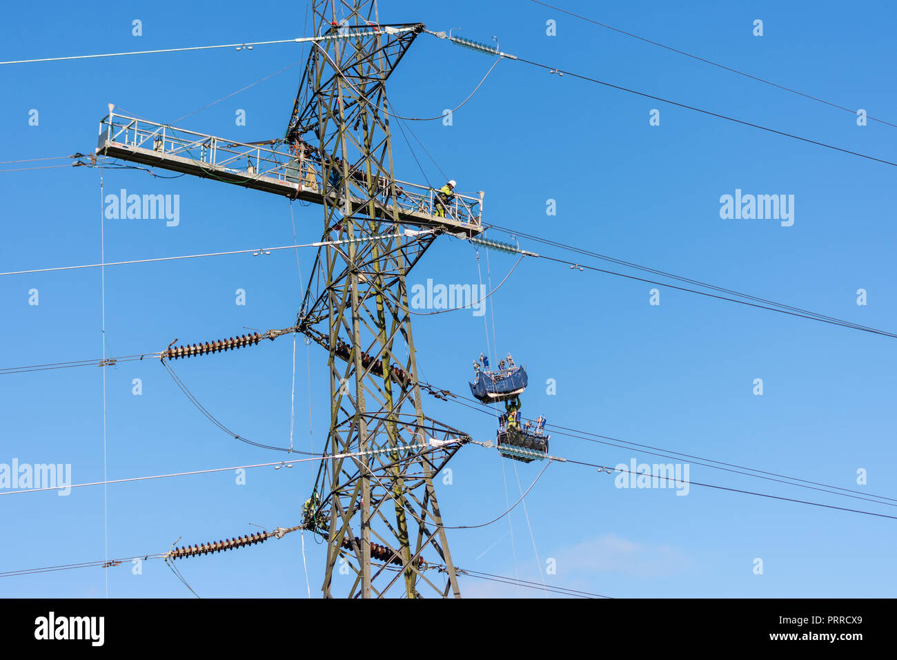 Workers replacing high voltage electricity cable on a pylon using platforms and baskets suspended from the pylon Stock Photo