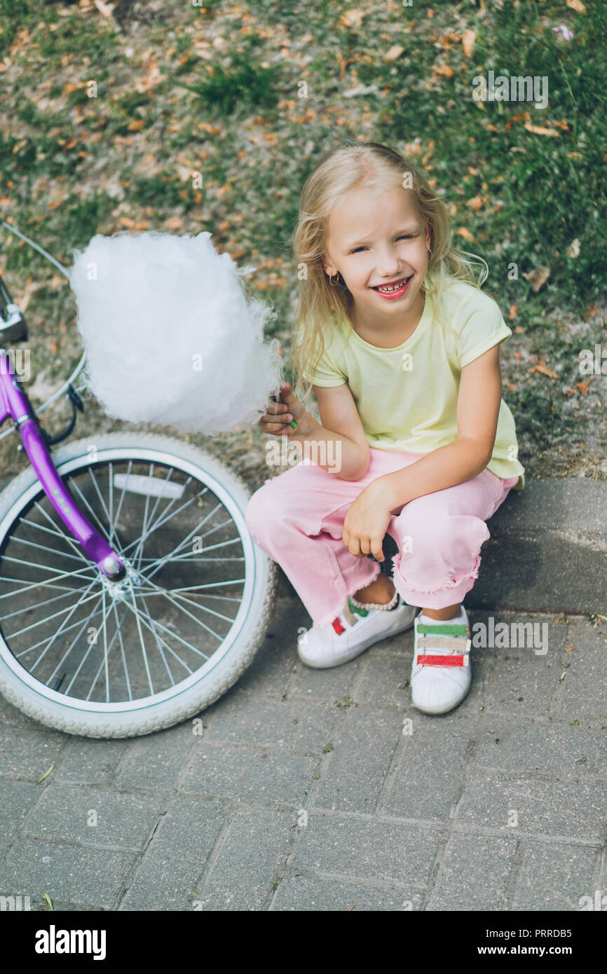 cheerful kid with cotton candy sitting on border in park Stock Photo