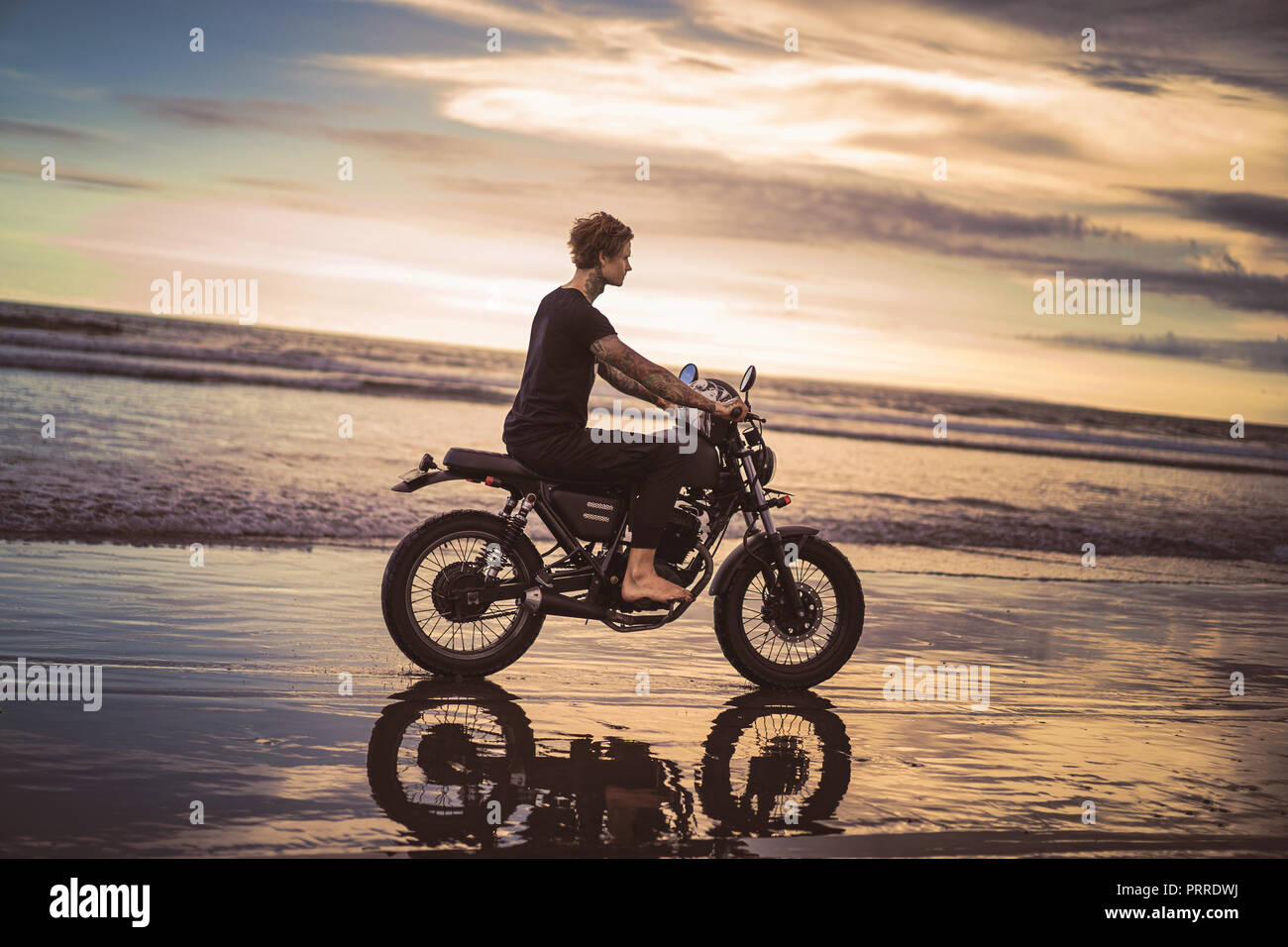 Beach Rode Side Profile side view of tattooed man riding motorbike on ocean beach during ...