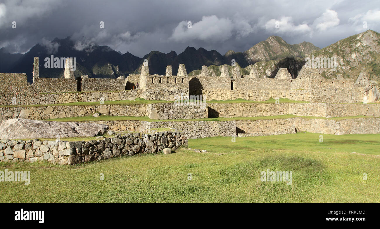 Inca stone structure ruins in bright sunlight with dark mountains in shade Stock Photo