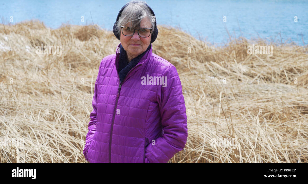 Serious female elder looking at camera with hands in pockets outdoors Stock Photo