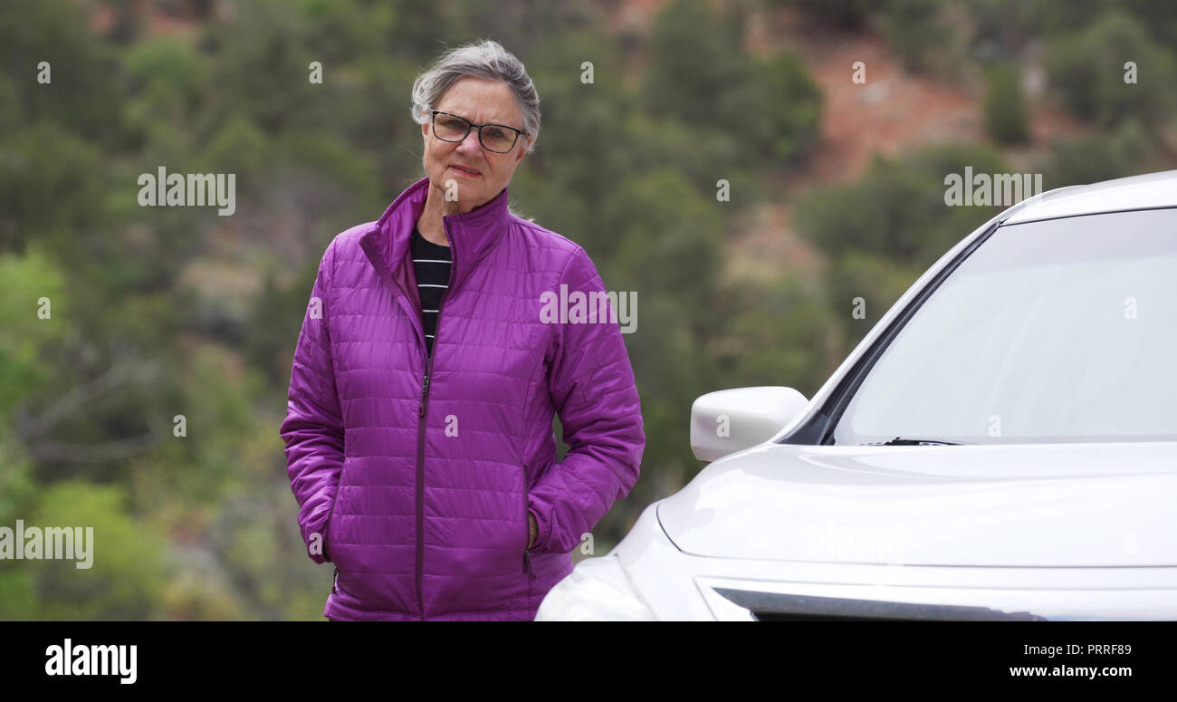 Somber elderly woman next to car looking at camera Stock Photo