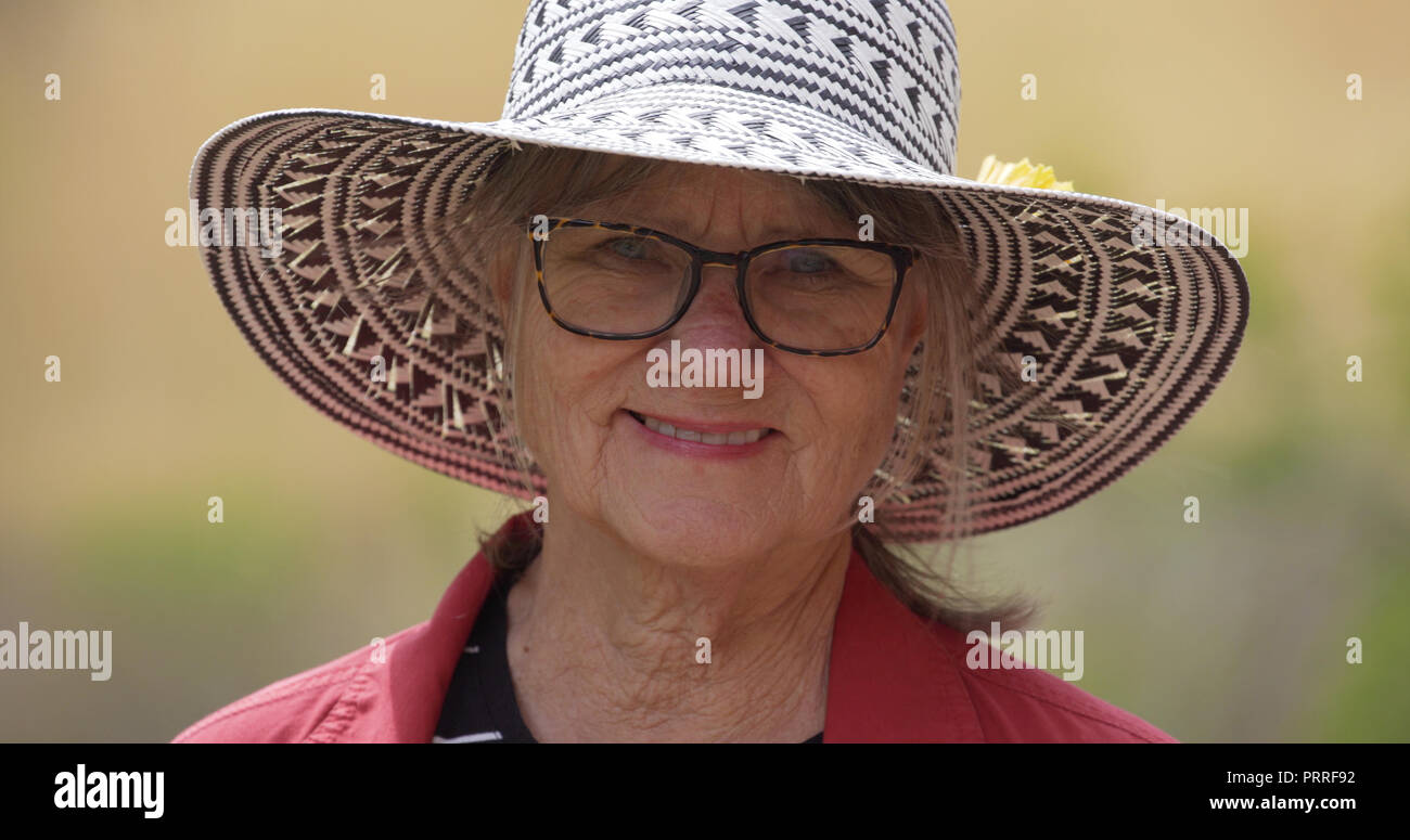 Close-up portrait of happy senior woman wearing hat and eyeglasses outdoors Stock Photo