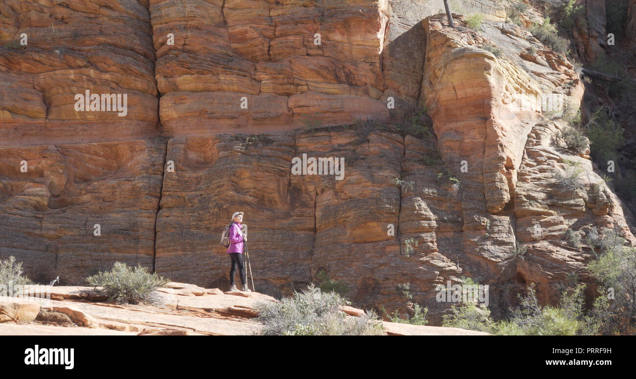Elderly female hiker taking break from walking to admire large sandstone cliff Stock Photo