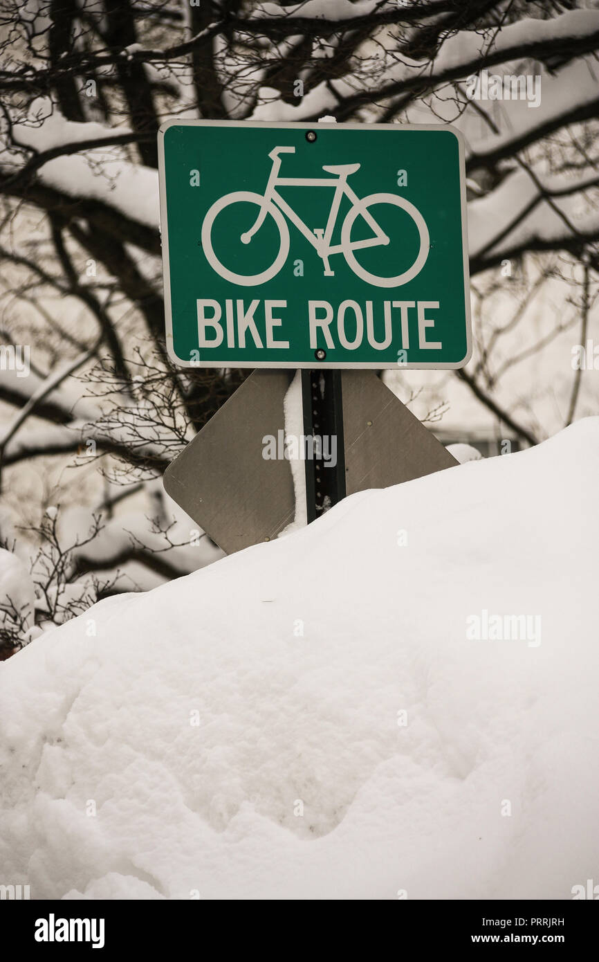 'Bike Route' sign almost buried in deep snow pile. Stock Photo