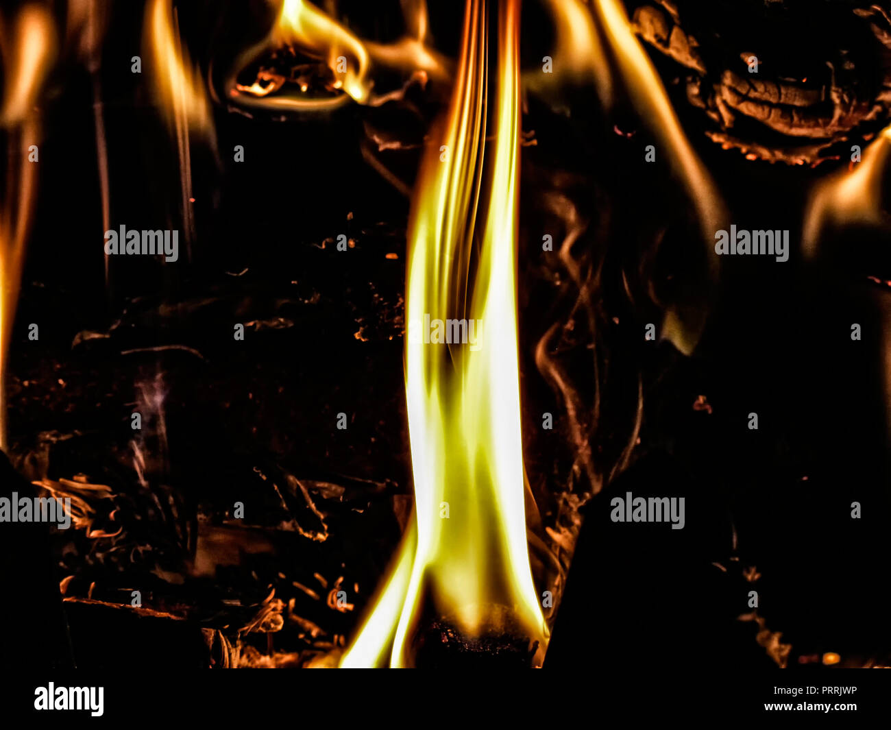 Closeup of fireplace fire with dominant foreground flame against dark background, flames and embers. Stock Photo