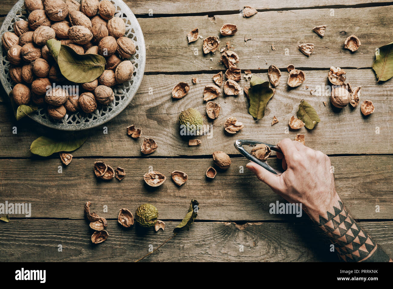 cropped shot of person holding nutcracker above wooden table with walnuts and nutshells Stock Photo