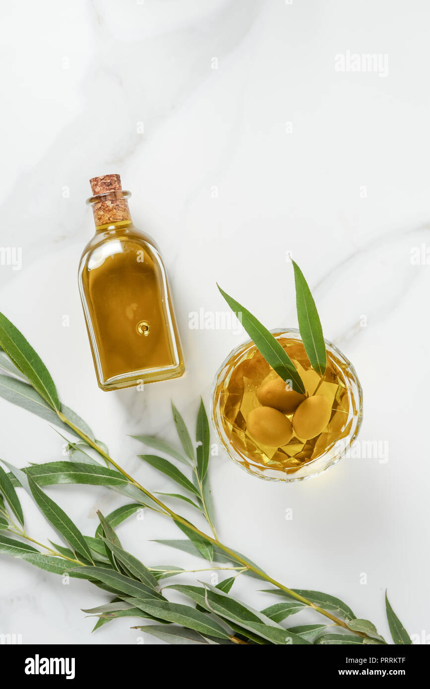 elevated view of bottle and glass with olive oil on marble tabletop ...
