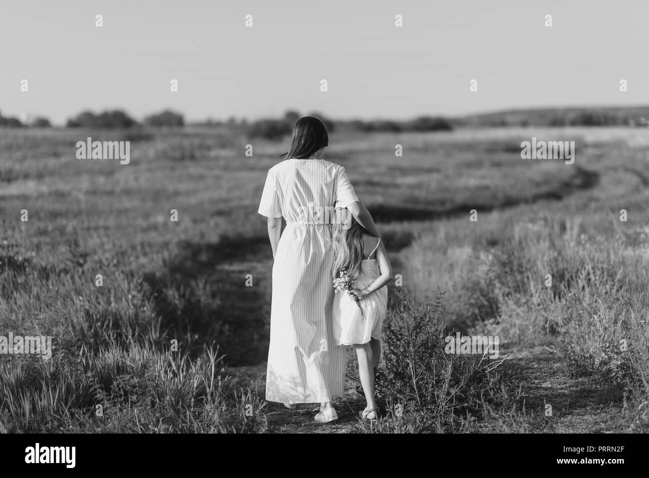 black and white shot of mother and daughter walking by rural road in green meadow Stock Photo