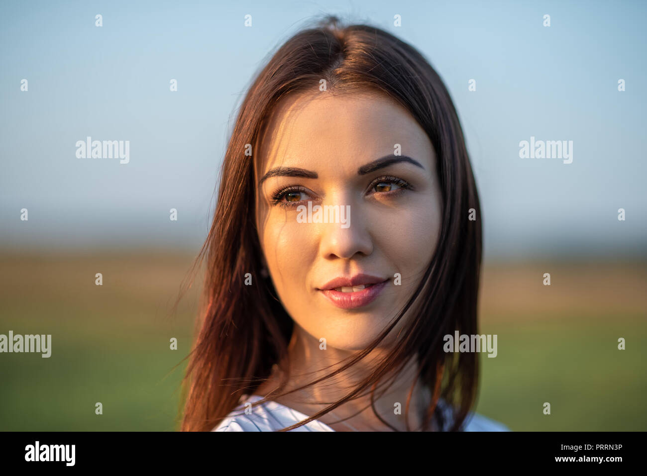 close-up portrait of beautiful young woman on green field under sunset ...
