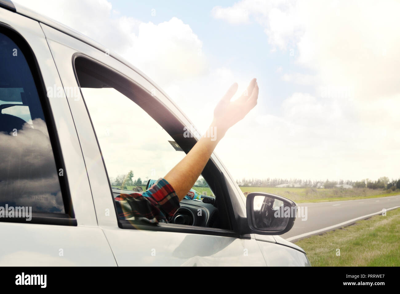 Woman sticking arm out of the car window on roadtrip. Female driver