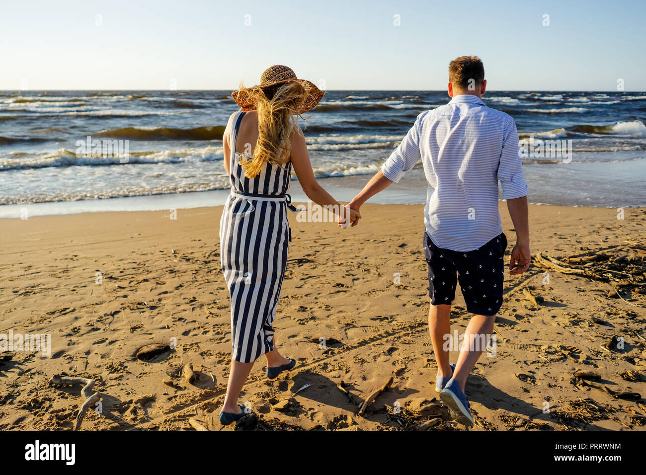 rear view of affectionate couple holding hands and walking on sandy ...