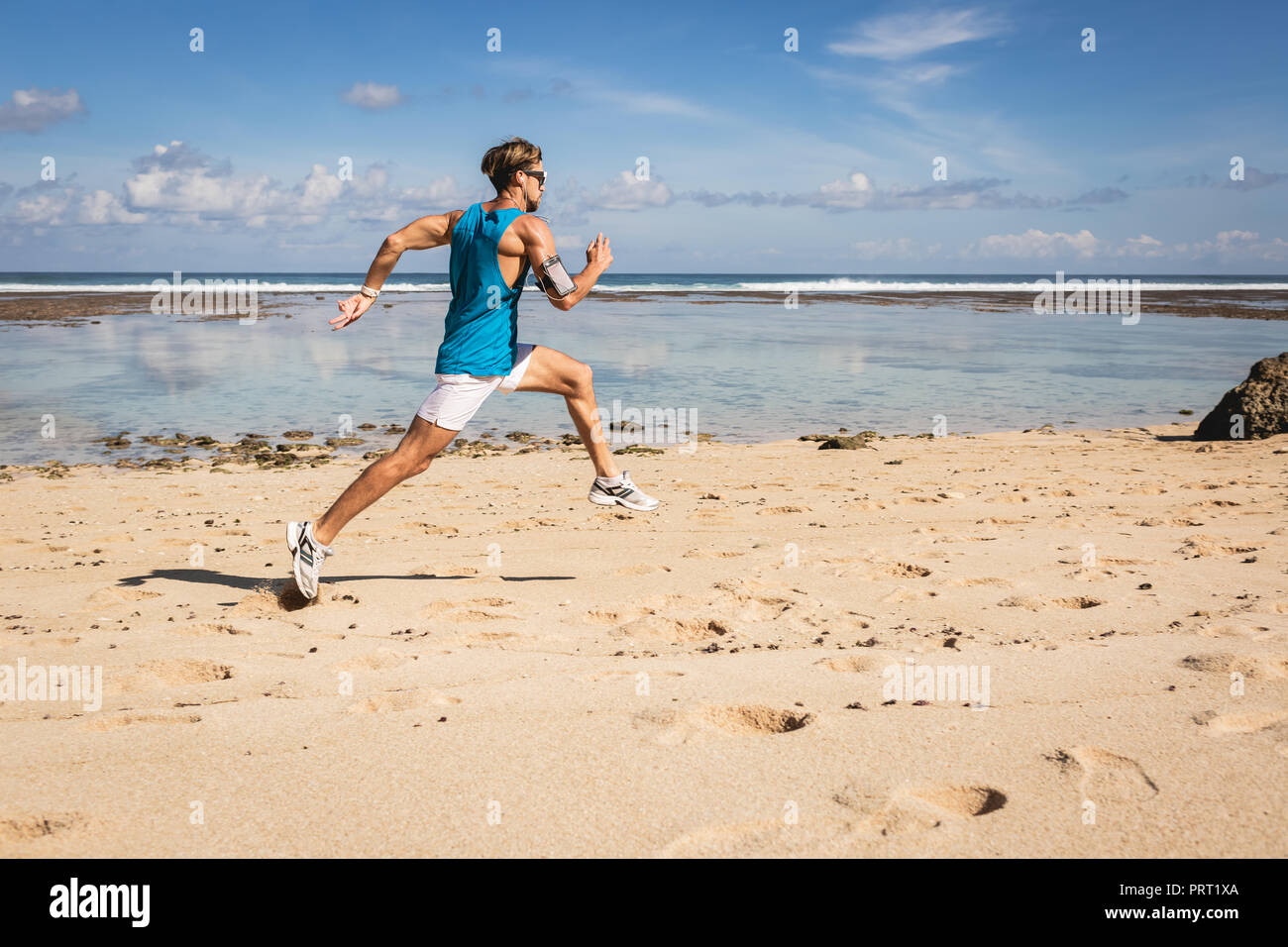 athletic man running and jumping on sand beach near sea, Bali, Indonesia Stock Photo