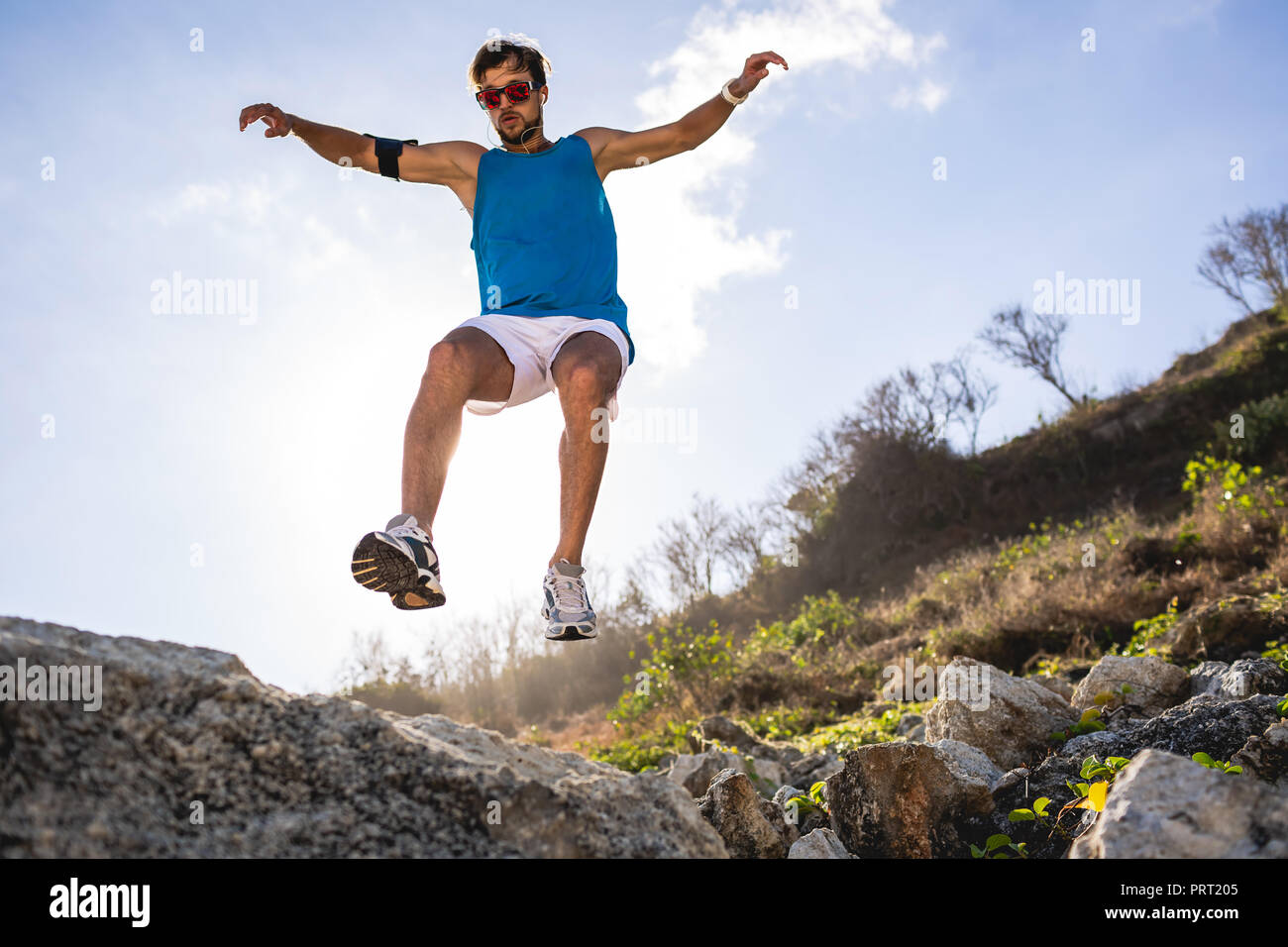 bottom view of athletic man jumping from rocks with sunlight Stock Photo