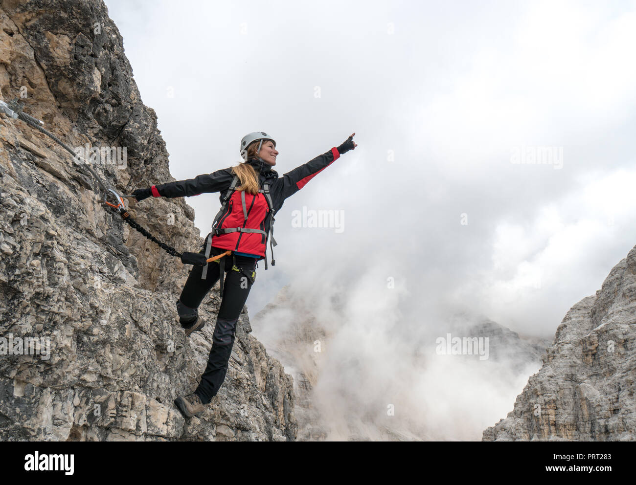 young female climber on a vertical and exposed rock face smiling and