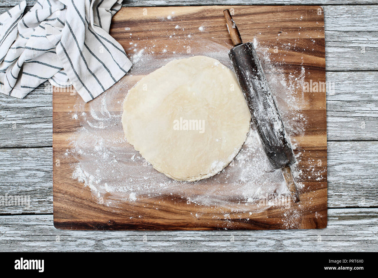 Homemade butter pie crust dough with rolling pin and towel over floured rustic wooden background. Image shot from overhead. Stock Photo
