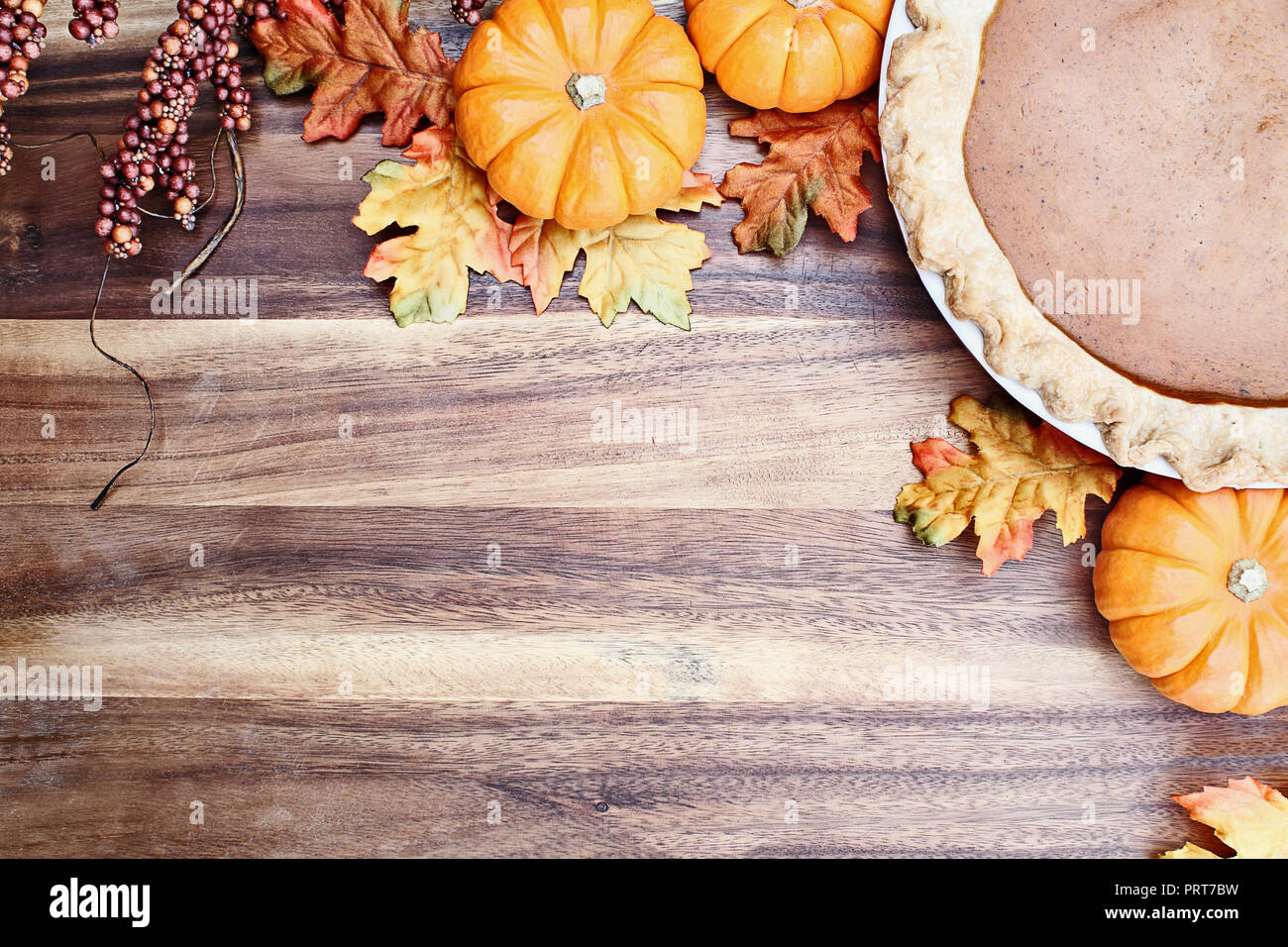 Homemade pumpkin pie in pie plate with little pumpkins, autumn leaves and room for text over rustic wooden background. Image shot from overhead. Stock Photo