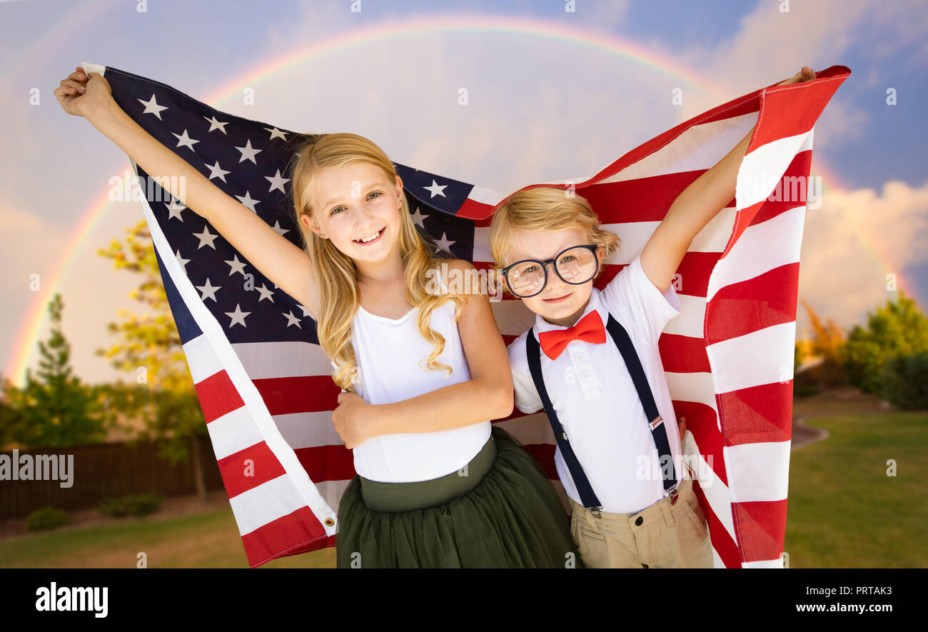 Cute Young Cuacasian Boy and Girl Holding American Flag With Rainbow Behind. Stock Photo