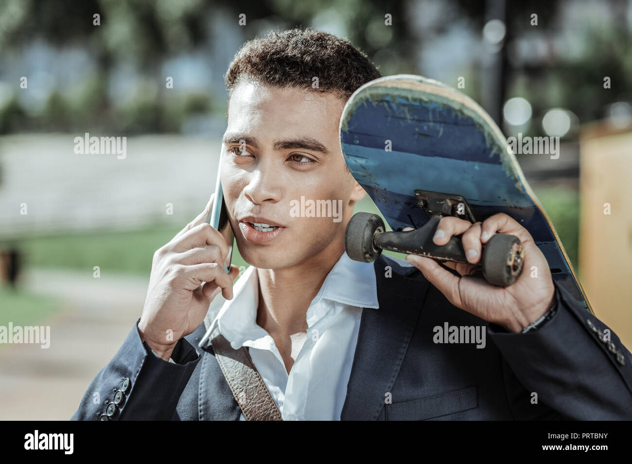 Charming male student calling friends with skateboard Stock Photo