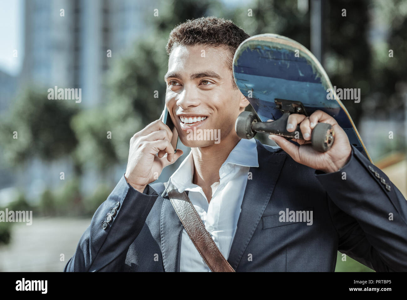 Cheerful male student telephoning friends with skateboard Stock Photo