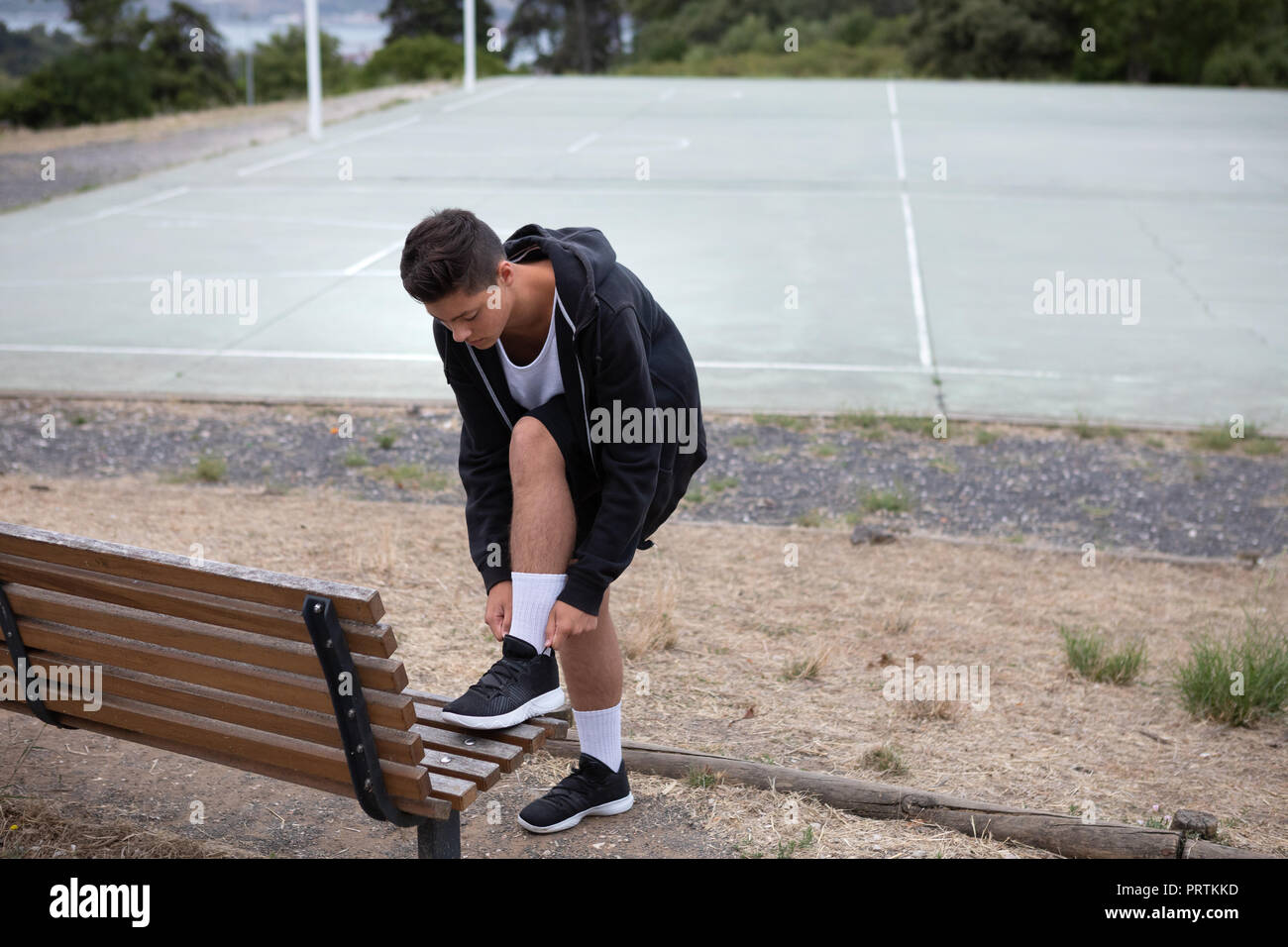 Male teenage basketball player fastening trainers by basketball court Stock Photo