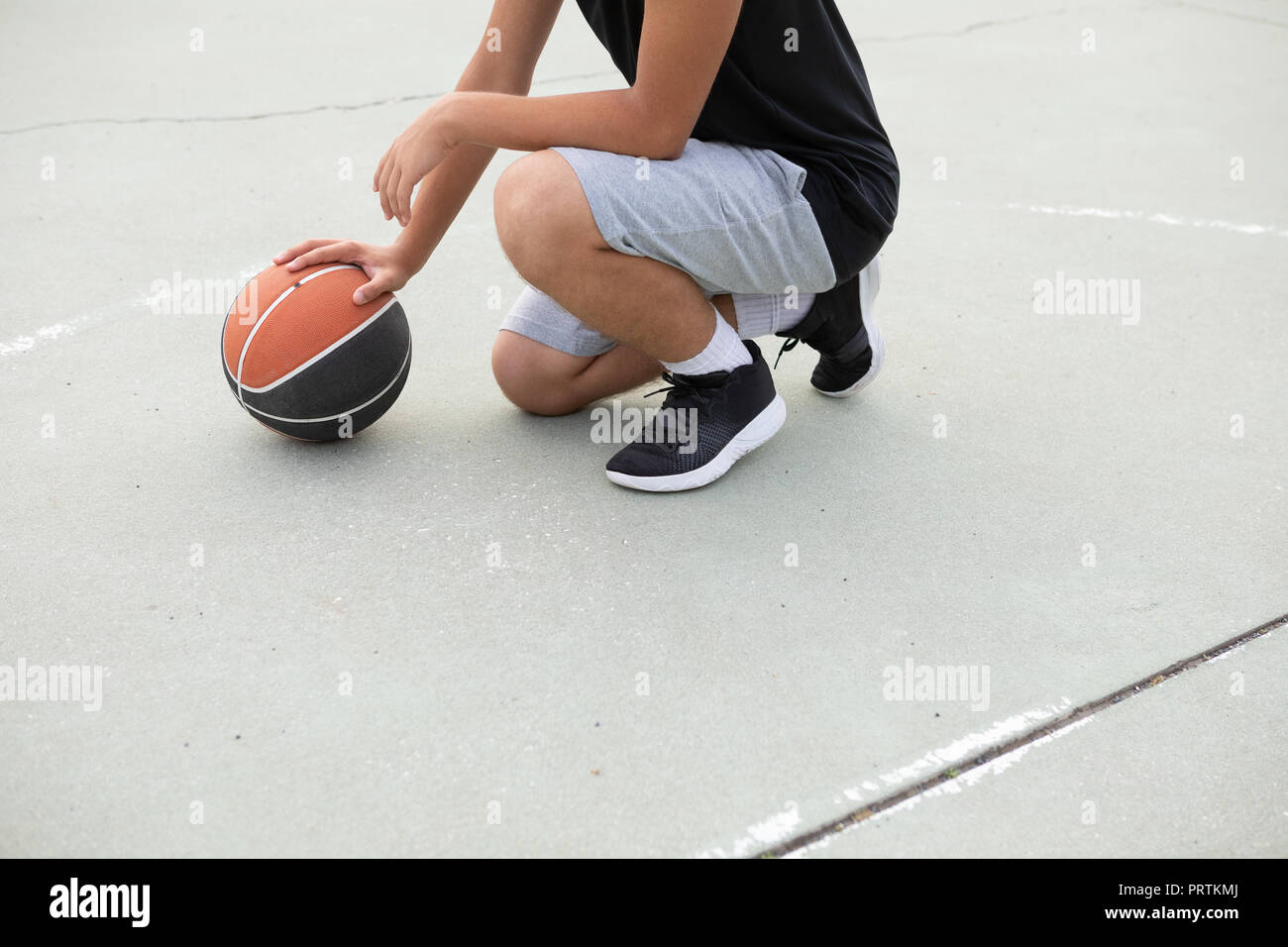 Male teenage basketball player crouching with ball on basketball court, neck down Stock Photo