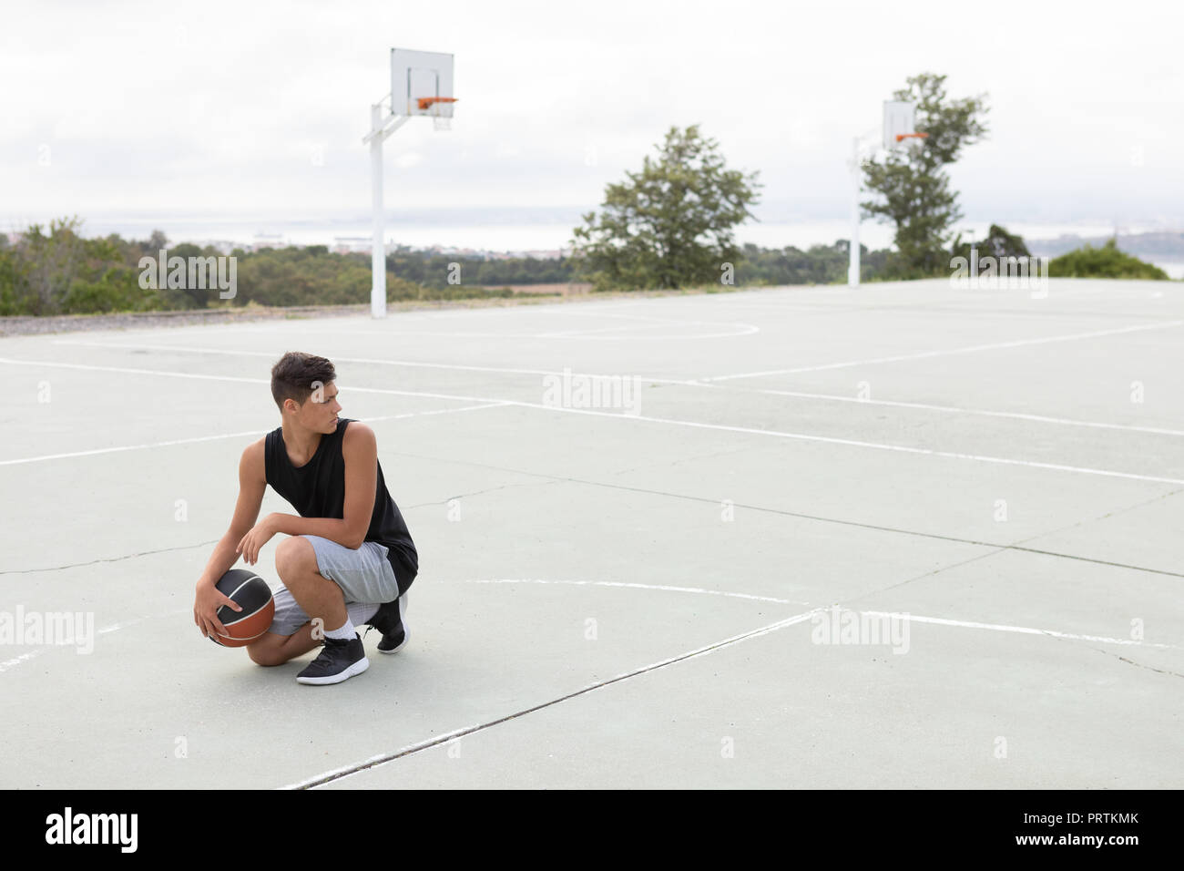 Male teenage basketball player crouching with ball on basketball court Stock Photo