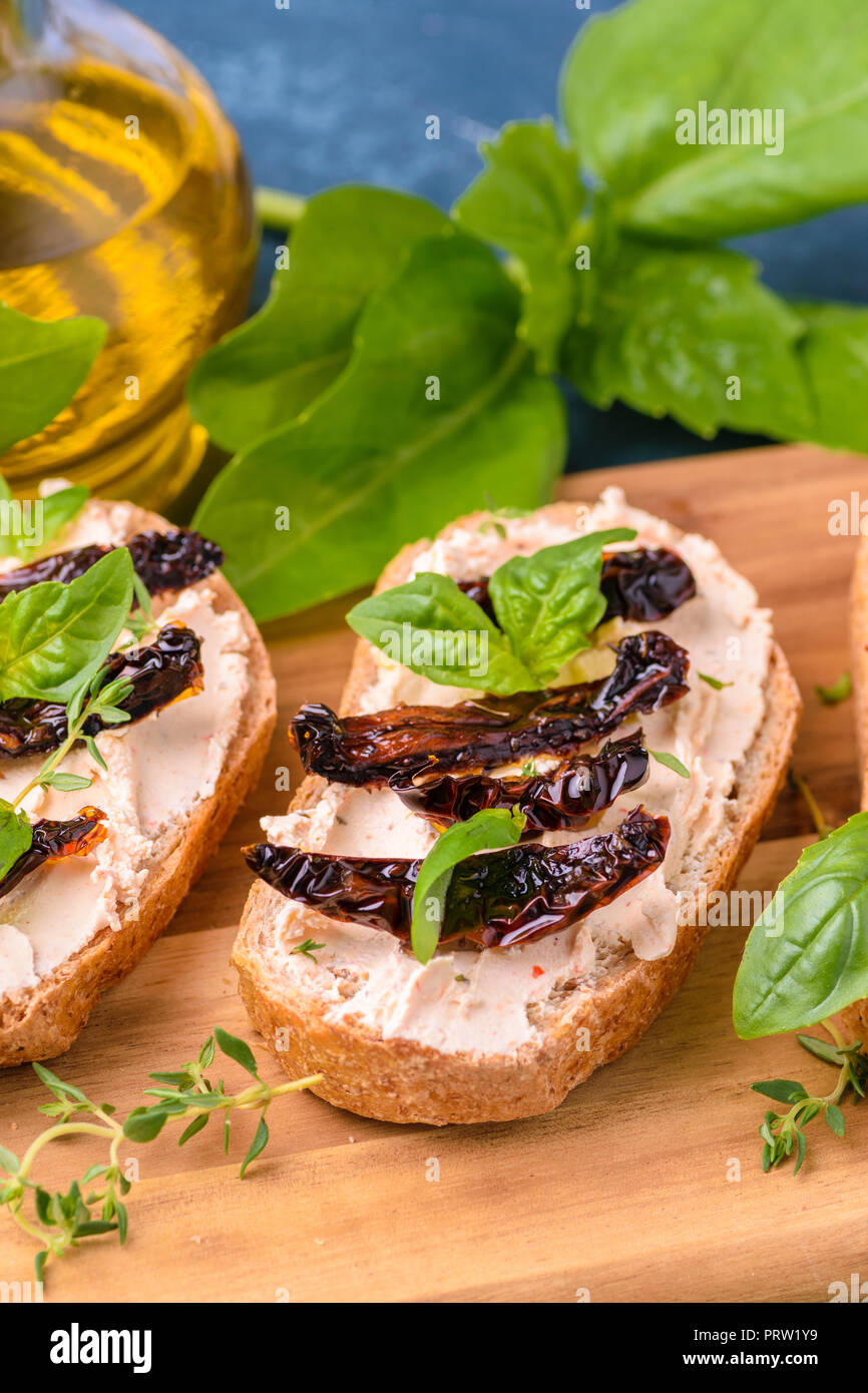 Toast sandwich (bruschetta) with cream cheese, slices of dried tomato and basil leaves. On wooden board. Delicious meal. Stock Photo