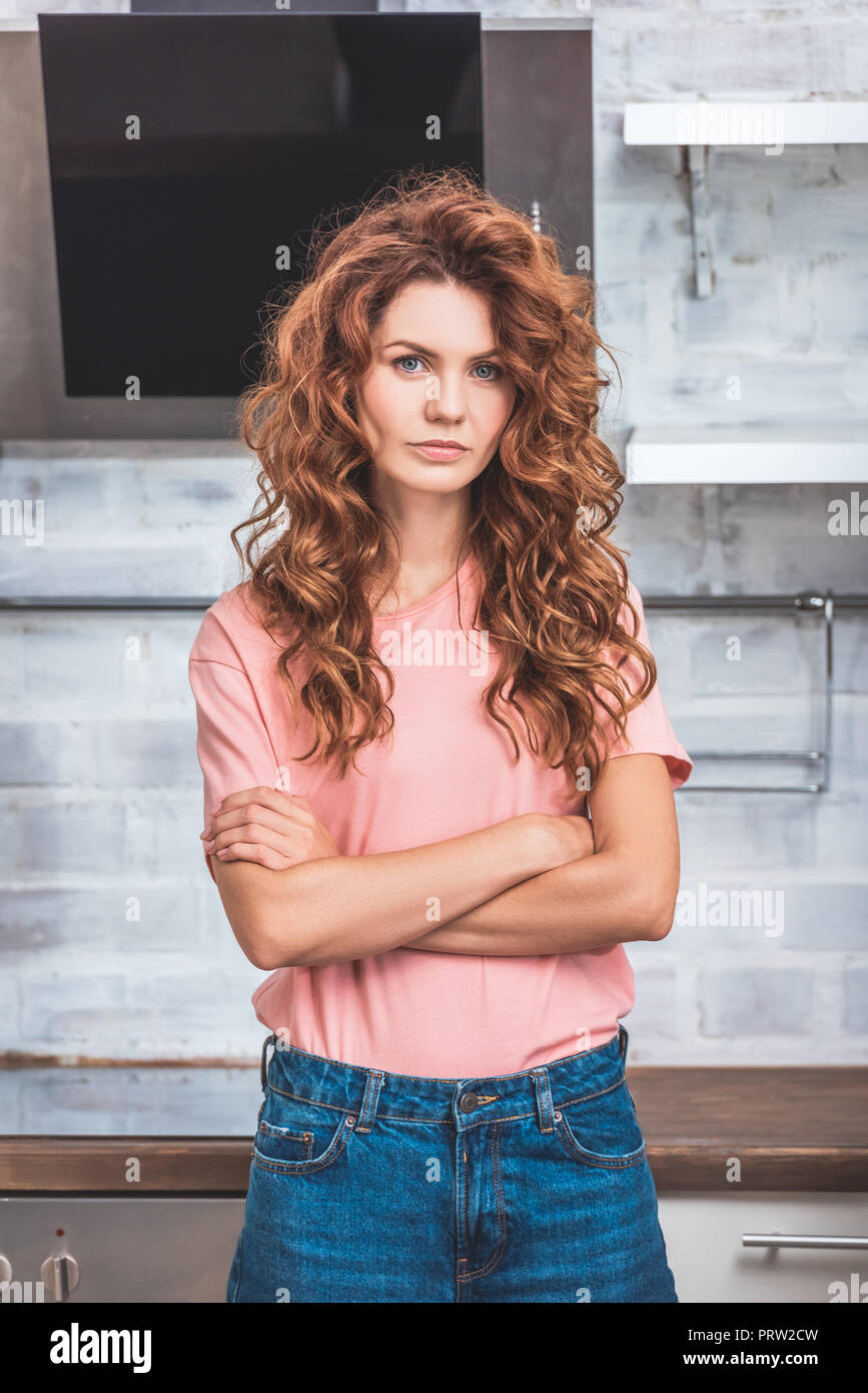 beautiful woman with red curly hair standing with crossed arms near cardboard boxes at new kitchen and looking at camera Stock Photo
