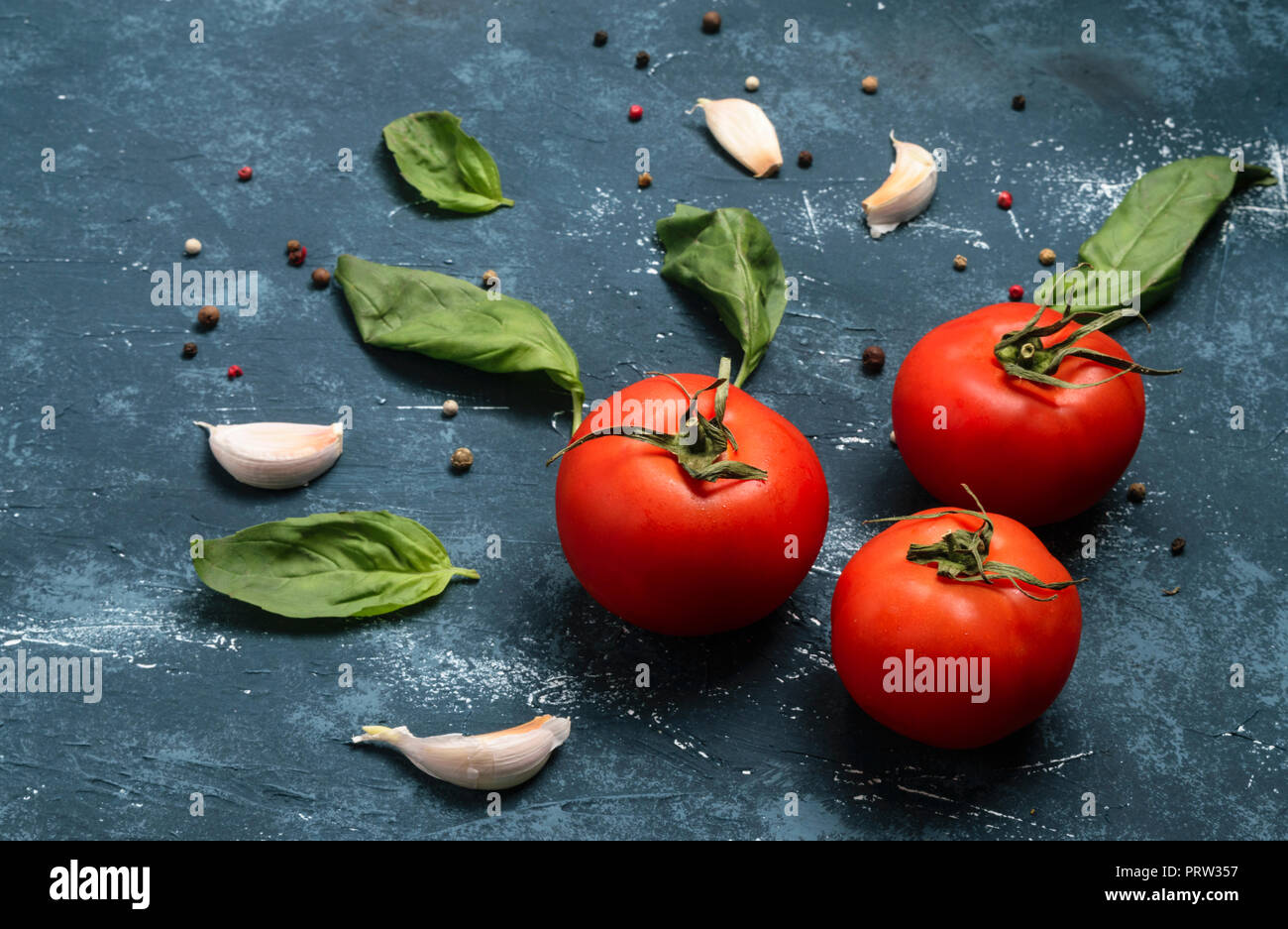 Cooking  ingredients - basil leaves, garlic cloves, pepper and tomatoes. Concrete grunge background. Stock Photo