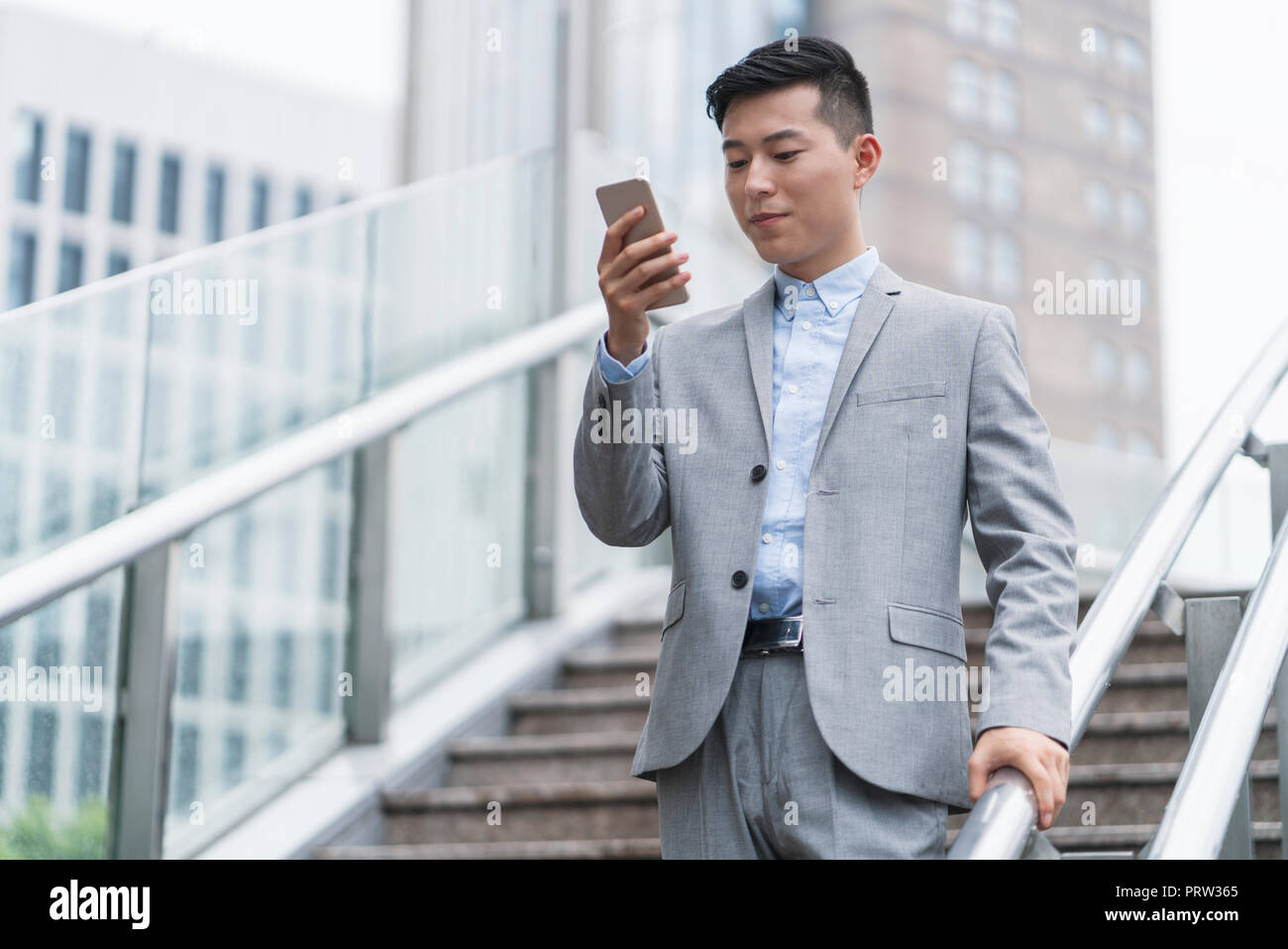 Young businessman looking at smartphone on city stairway, Shanghai, China Stock Photo