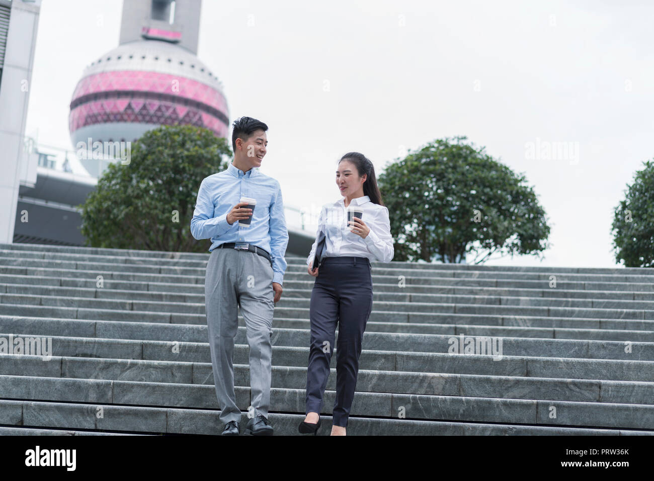 Young businesswoman and man with takeaway coffee moving down city stairway, Shanghai, China Stock Photo