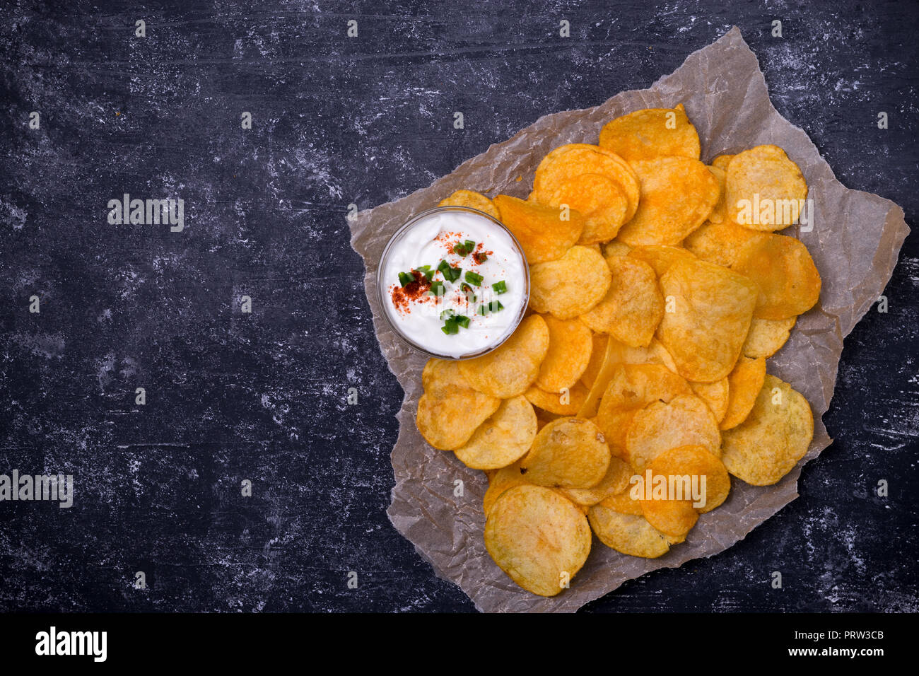 Potato chips with dip on parchment paper. Dark concrete background. Top view Stock Photo