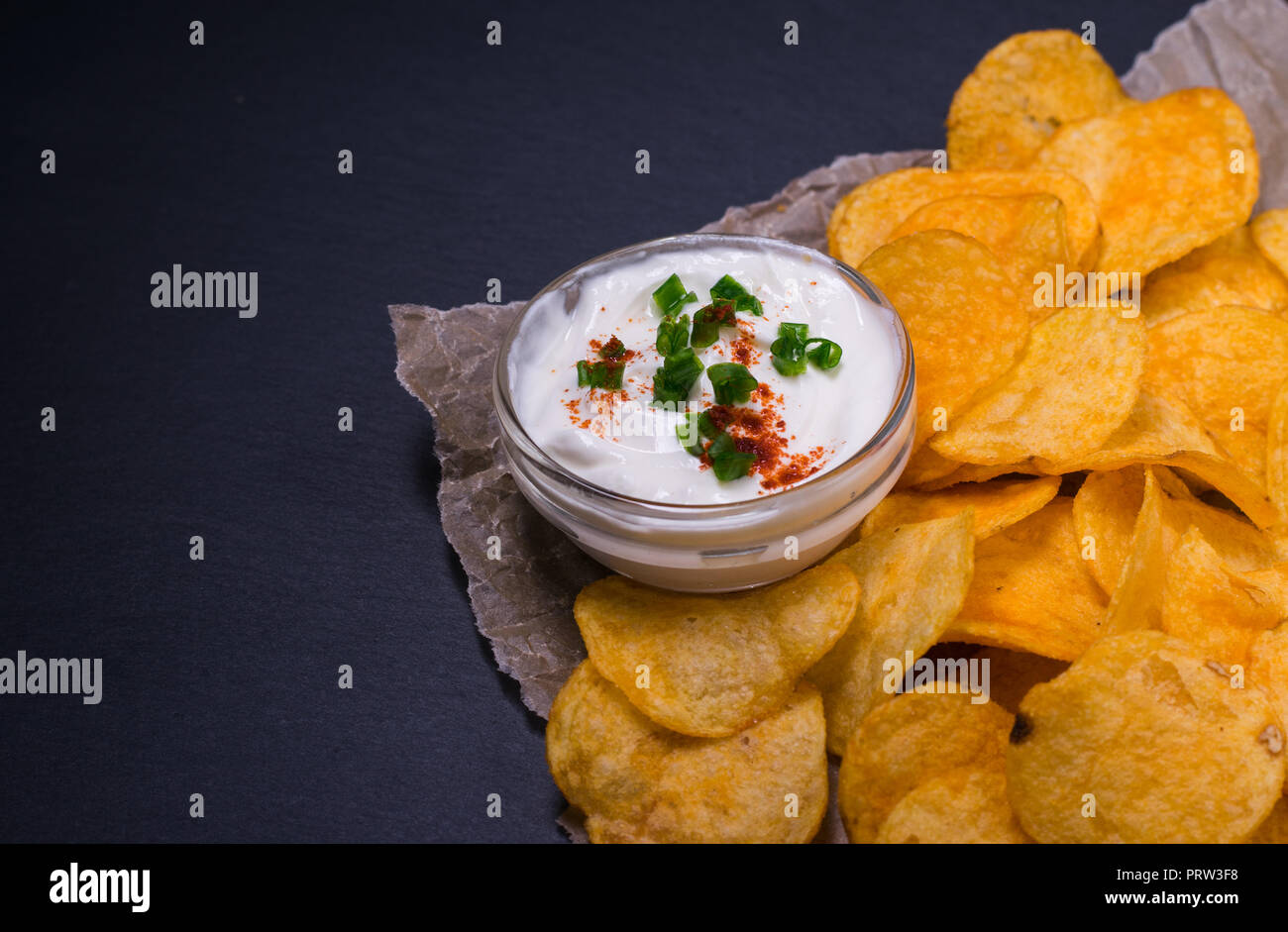 Potato chips with dip on parchment paper. On dark black stone table background Stock Photo