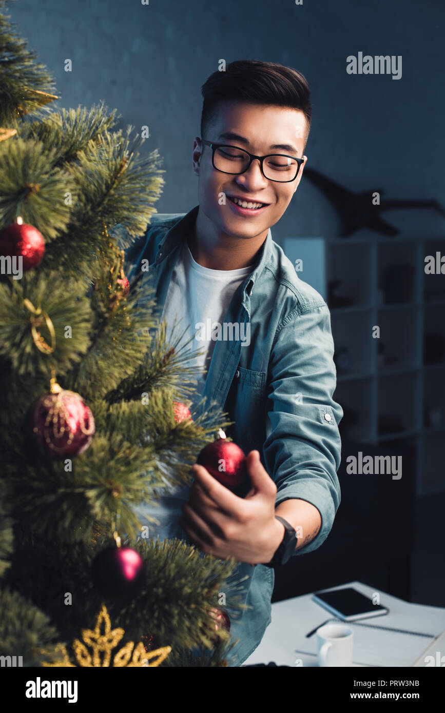 handsome smiling young asian man decorating christmas tree at home Stock Photo