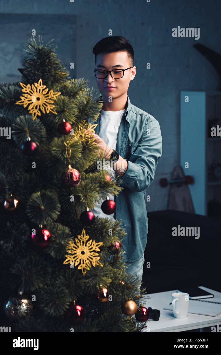 young asian man in eyeglasses decorating christmas tree at home Stock Photo