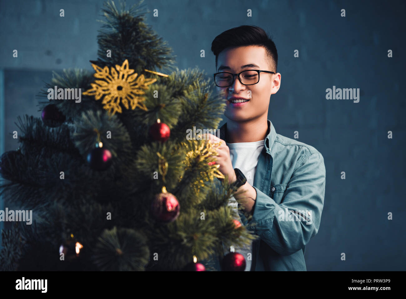 smiling young asian man in eyeglasses decorating christmas tree at home Stock Photo