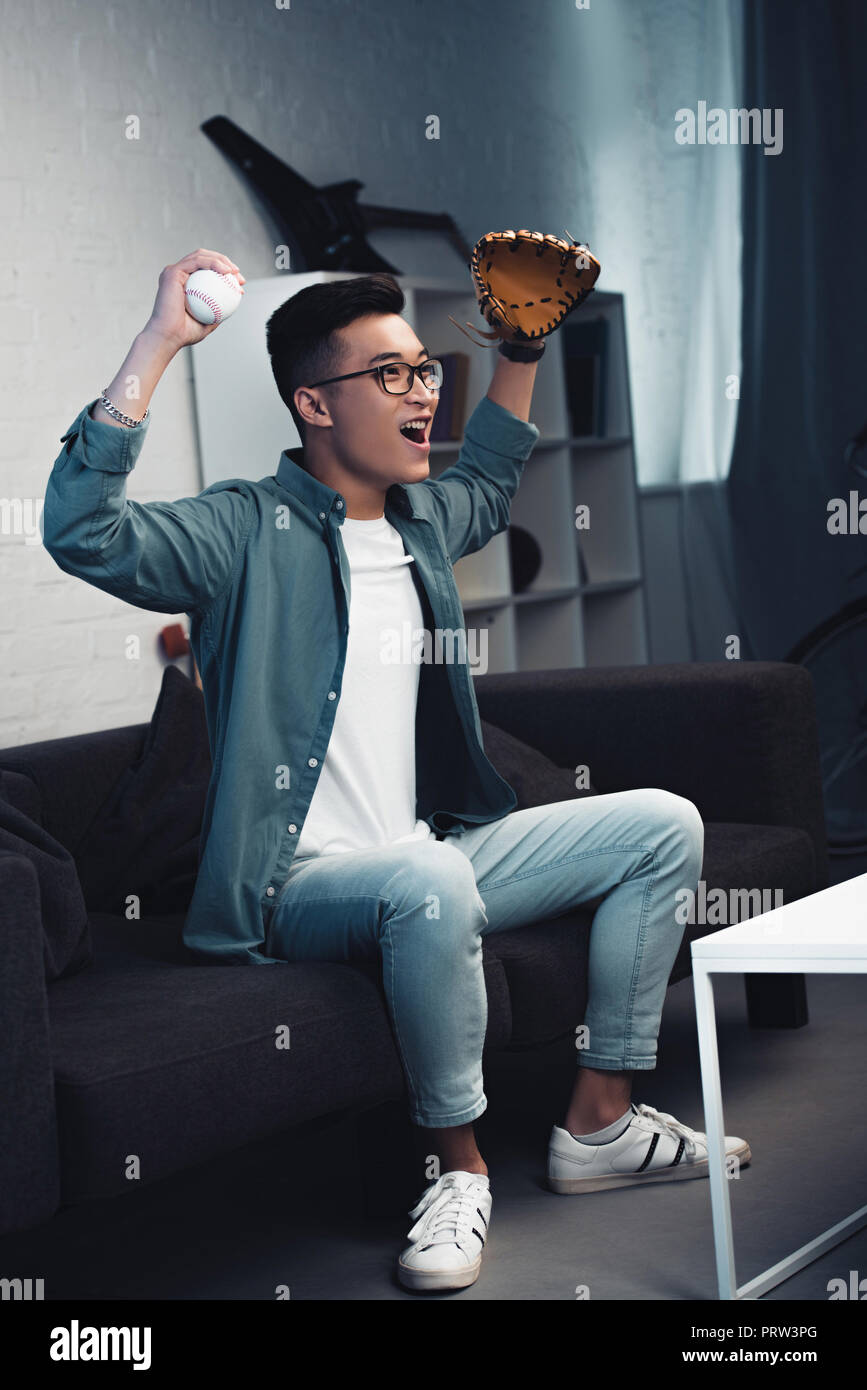 Excited Young Man With Baseball Glove And Ball Sitting On Couch