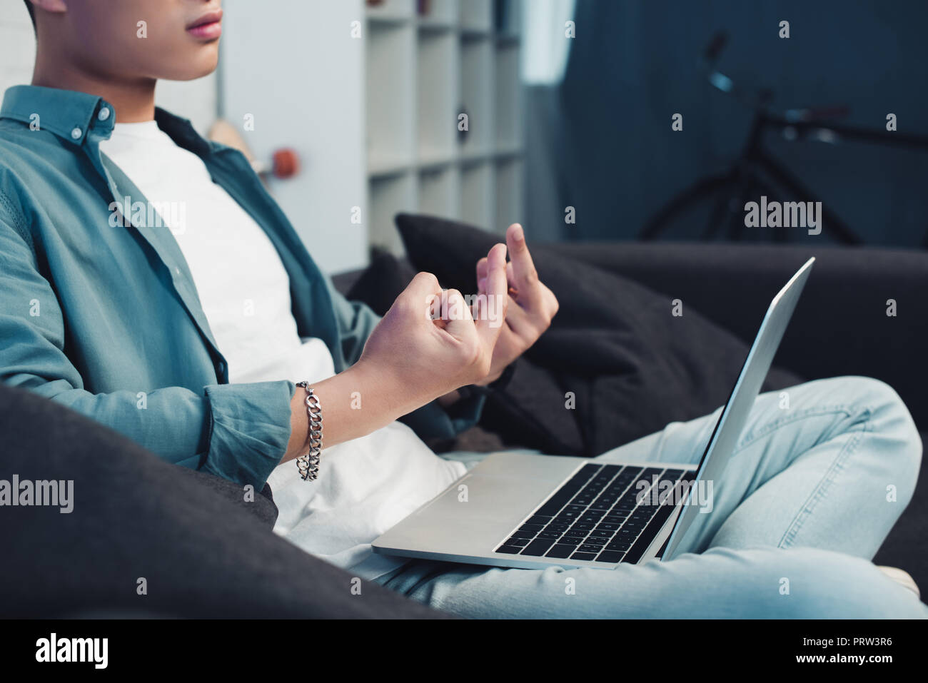 cropped shot of young man sitting on couch and giving middle fingers to laptop Stock Photo